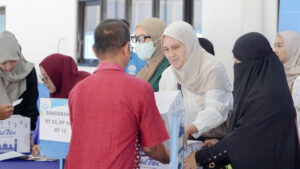 Potret seorang parent siswa Primary tengah menyerahkan paket baksos kepada warga