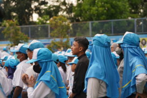 Seorang guru berdiri di dekat barisan untuk mendampingi dan mengawasi siswa-siswanya